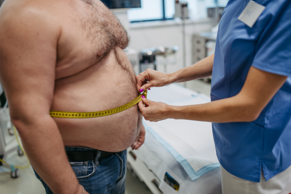 Female doctor measuring waist of overweight patient using a tape measure. Obesity affecting middle-aged men's health. Concept of health risks of overwight and obesity.