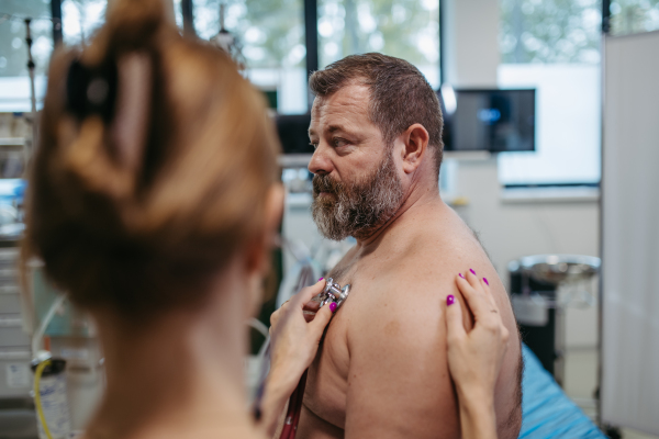 Female doctor listening to the heartbeats and rhytm of overweight patient using stethoscope. Obesity affecting middle-aged men's health. Concept of health risks of overwight and obesity.