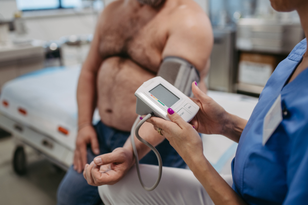 Doctor measuring blood pressure, examining hypertension, using blood pressure monitor. Obesity affecting middle-aged men's health. Concept of health risks of overwight and obesity.