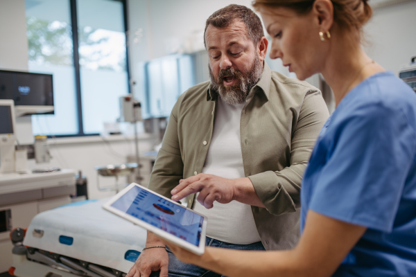 Female doctor consulting with the overweight patient, discussing test result in doctor office. Obesity affecting middle-aged men's health. Concept of health risks of overwight and obesity.