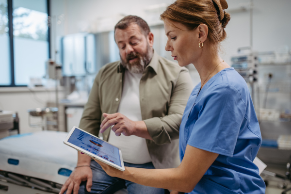 Female doctor consulting with the overweight patient, discussing test result in doctor office. Obesity affecting middle-aged men's health. Concept of health risks of overwight and obesity.