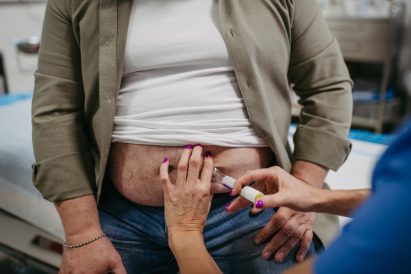 Doctor is injecting insulin into a patient's abdomen using insulin pen. Obese, overweight man is at risk of developing type 2 diabetes. Concept of health risks of overwight and obesity.