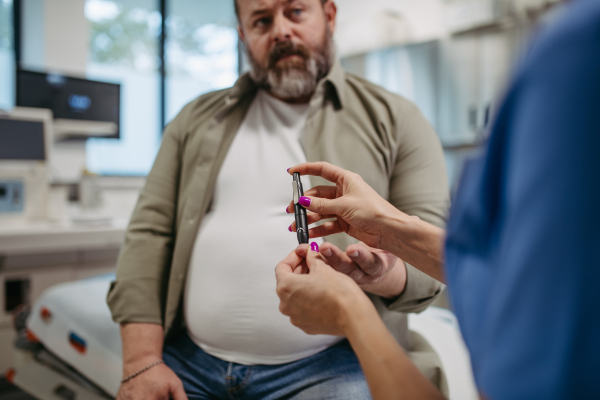 Nurse checking man's blood glucose level using a fingerstick glucose meter. Obese or overweight man at risk of developing type 2 diabetes. Concept of health risks of overwight and obesity.