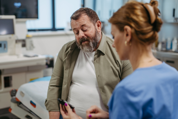 Doctor checking blood glucose level using a fingerstick glucose meter, waiting for results from glucometer. Obese or overweight man at risk of developing type 2 diabetes. Concept of health risks of overwight and obesity.