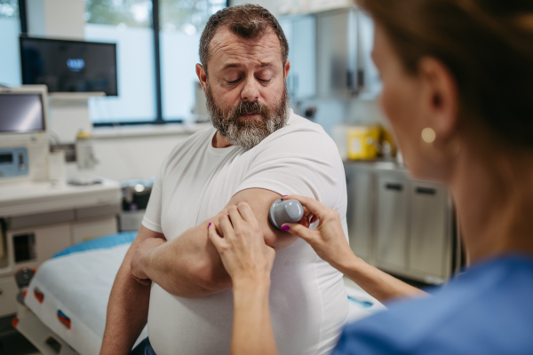 Doctor applying a continuous glucose monitor sensor on patient's arm. Obese or overweight man is at risk of developing type 2 diabetes. Concept of health risks of overwight and obesity.