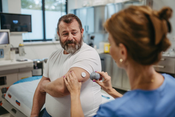 Doctor applying a continuous glucose monitor sensor on patient's arm. Obese or overweight man is at risk of developing type 2 diabetes. Concept of health risks of overwight and obesity.