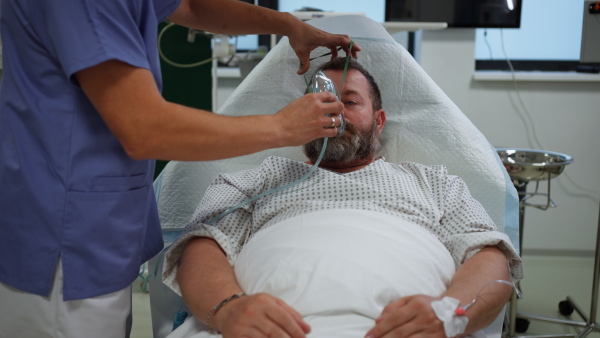 Nurse fitting an oxygen mask on patient in hospital bed. Man in intensive care unit in hospital.