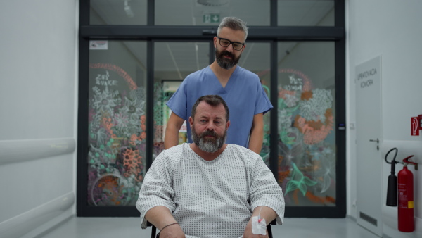 Male nurse pushing a patient in wheelchair along a hospital corridor. Overweight patient feeling anxious and has health concerns.