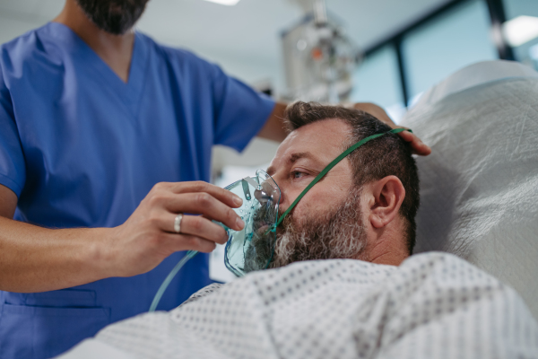 Nurse fitting an oxygen mask on patient in hospital bed. Man in intensive care unit in hospital.