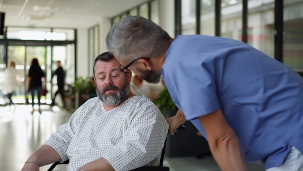 Male nurse pushing a patient in wheelchair along a hospital corridor. Overweight patient feeling anxious and has health concerns.