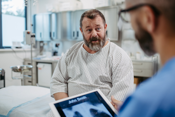 Doctor showing overweight patient chest x-ray, discussing test result in the emergency room. Respiratory diseases in middle-aged men's health. Concept of health risks of overwight and obesity.