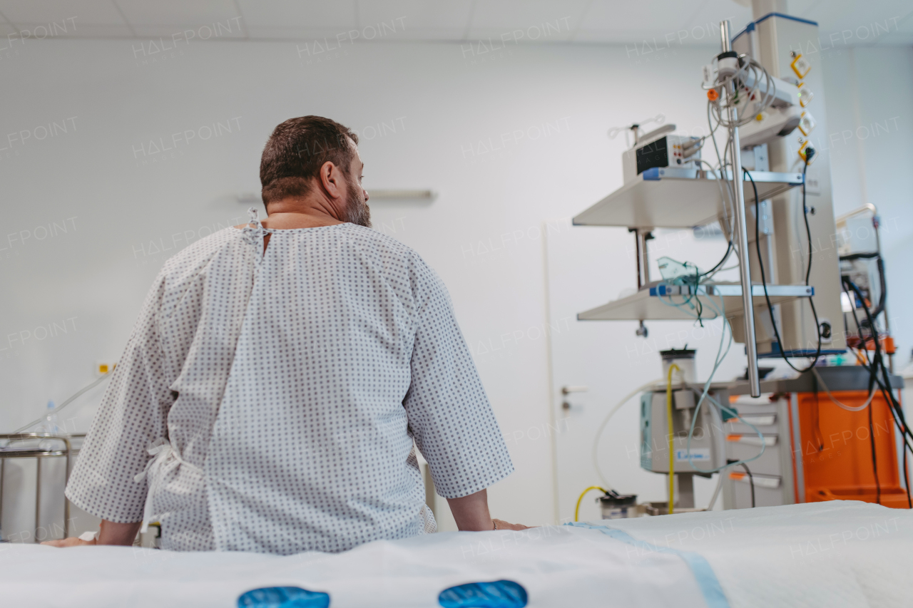 Rear view of overweight patient in hospital gown waiting for the medical examination, test results in hospital, feeling anxious, worried. Patient feeling dizzy, have vertigo and intense pain.