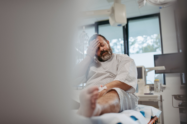 Overweight patient in hospital gown waiting for the medical examination, test results in hospital, feeling anxious. Patient feeling dizzy, have vertigo and intense pain.