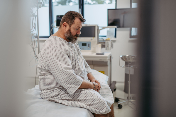 Overweight patient in hospital gown waiting for the medical examination, test results in hospital, feeling anxious, worried. Patient feeling dizzy, have vertigo and intense pain.