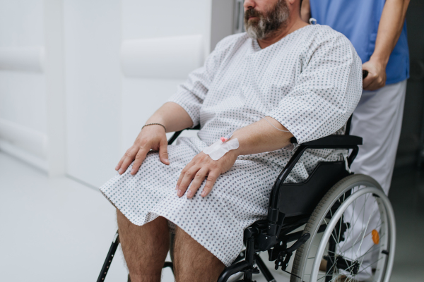 Male nurse pushing a patient in a wheelchair along a hospital corridor, waiting for a medical examination. Overweight patient feeling anxious and has health concerns.