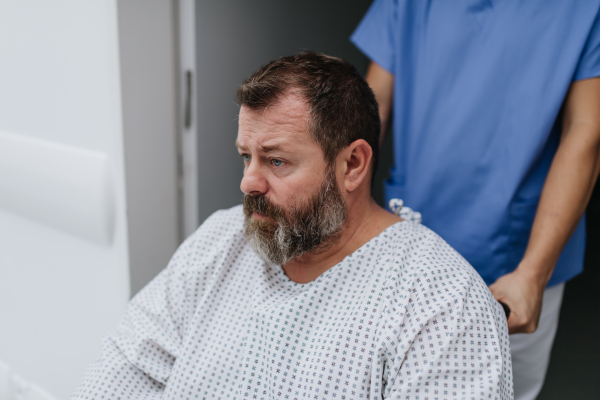 Male nurse pushing a patient in a wheelchair along a hospital corridor, waiting for a medical examination. Overweight patient feeling anxious and has health concerns.