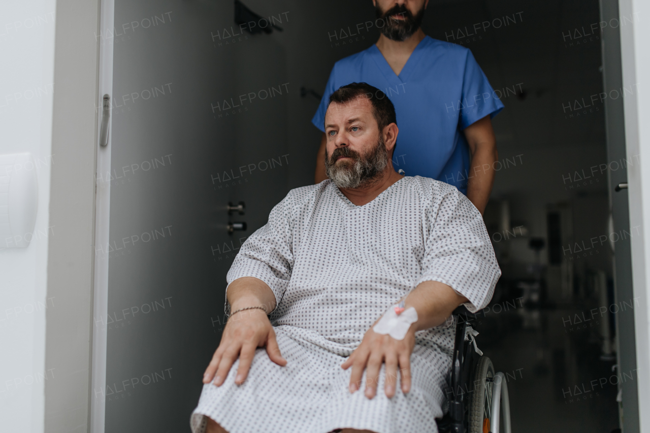 Male nurse pushing a patient in wheelchair along a hospital corridor. Overweight patient feeling anxious and has health concerns.