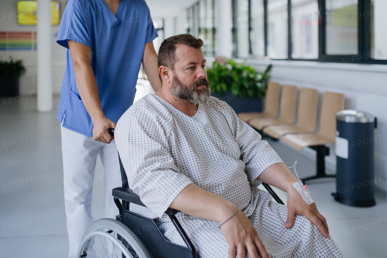 Male nurse pushing a patient in a wheelchair along a hospital corridor, waiting for a medical examination. Overweight patient feeling anxious and has health concerns.