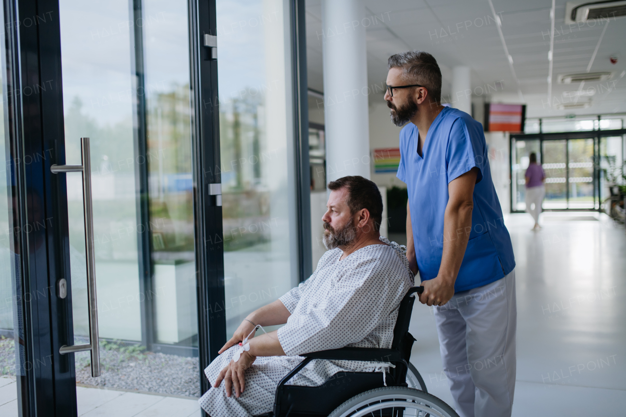 Male nurse pushing a patient in wheelchair along a hospital corridor. Overweight patient feeling anxious and has health concerns.