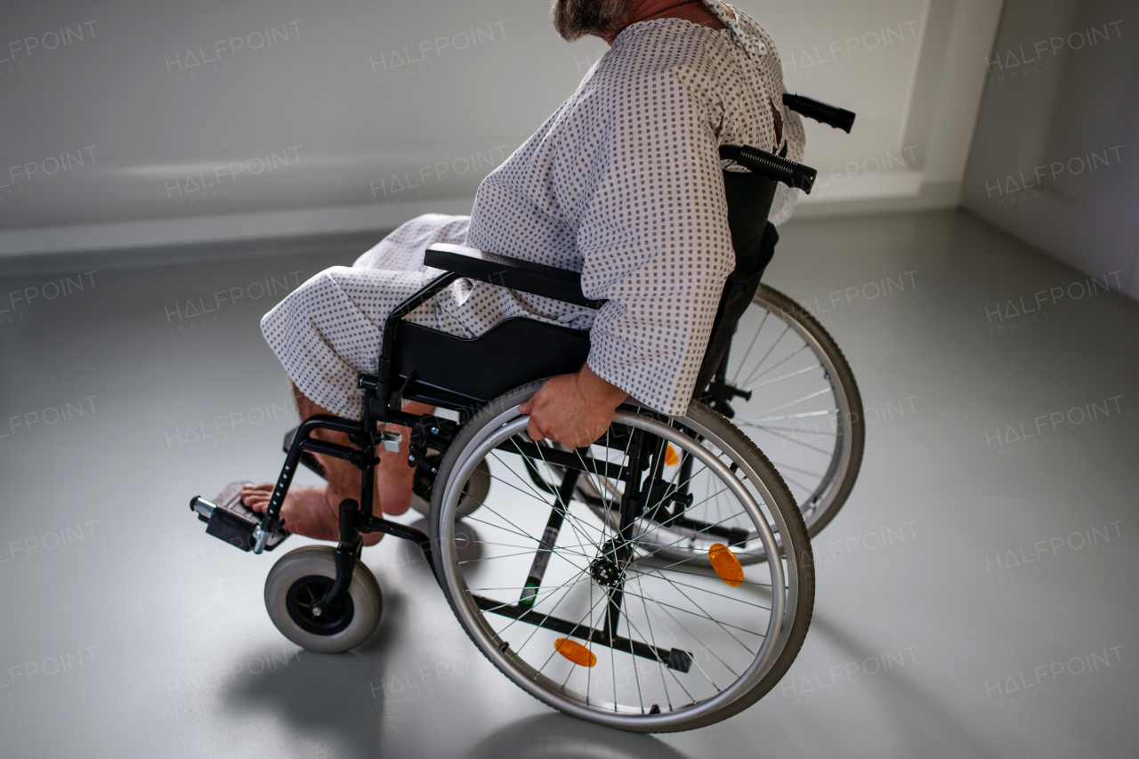 Side view of the man in wheelchair. Overweight patient in hospital gown waiting for medical examination in hospital.