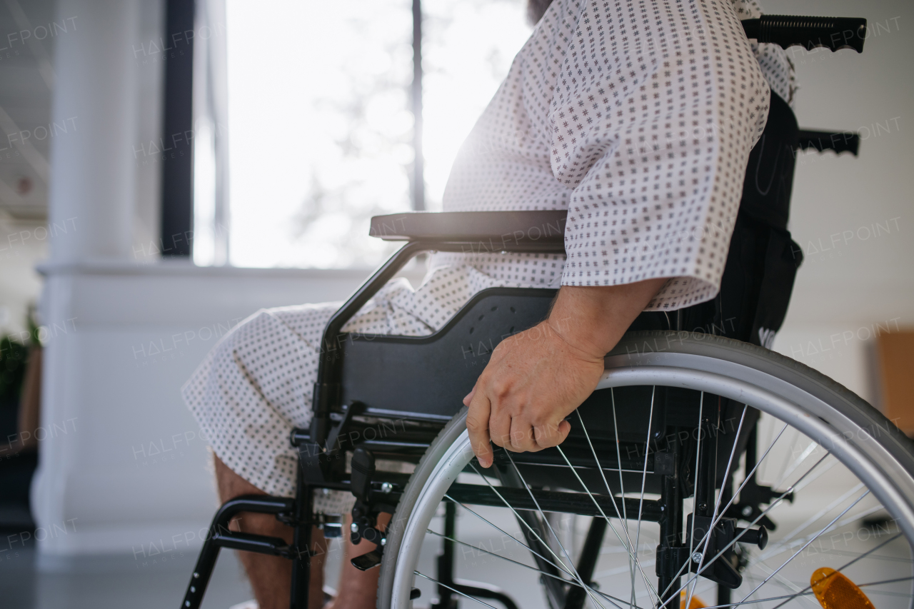 Side view of the man in wheelchair. Overweight patient in hospital gown waiting for medical examination in hospital.