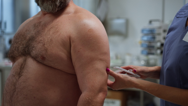 Female doctor measuring arm circumference of overweight patient. Obesity affecting middle-aged men's health. Concept of health risks of overwight and obesity.