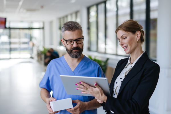 Pharmaceutical sales representative talking with doctor in medical building. Ambitious female sales representative presenting new medication, pills. Woman business leader.