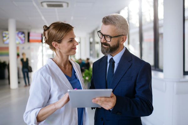 Pharmaceutical sales representative talking with the female doctor in medical building. Hospital director consulting with healthcare staff.