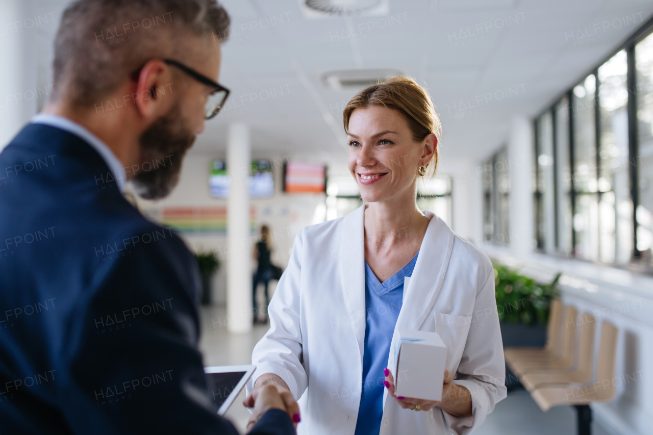 Pharmaceutical sales representative shaking hand with the female doctor in medical building. Hospital director consulting with healthcare staff.