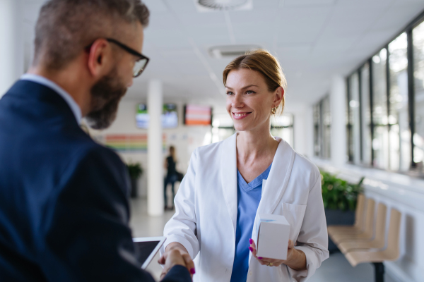 Pharmaceutical sales representative shaking hand with the female doctor in medical building. Hospital director consulting with healthcare staff.