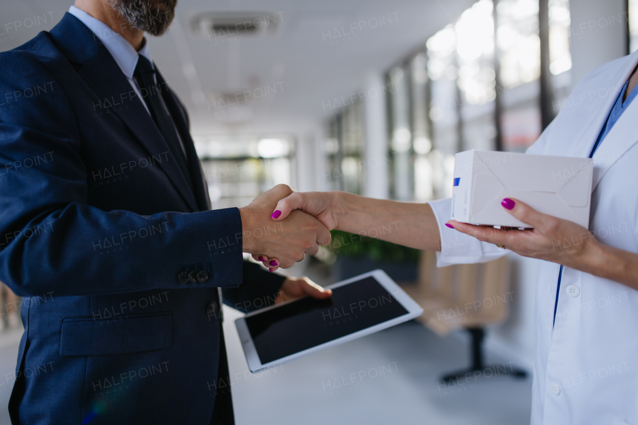 Pharmaceutical sales representative shaking hand with the female doctor in medical building. Hospital director consulting with healthcare staff.