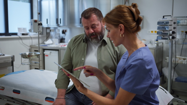 Female doctor consulting with the overweight patient, discussing test result in doctor office. Obesity affecting middle-aged men's health. Concept of health risks of overwight and obesity.