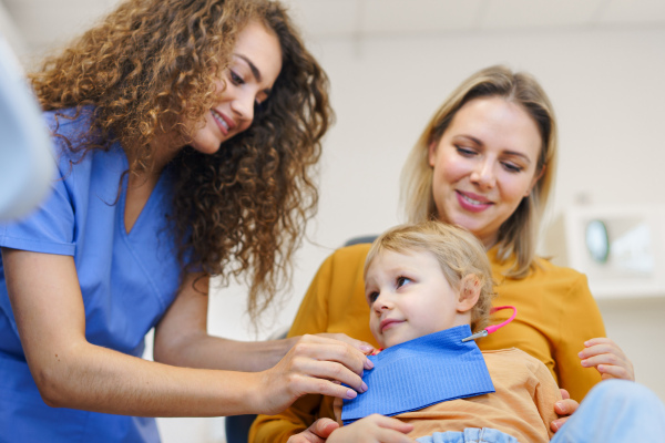 Little girl sitting with her mother on dentist chair, during preventive examination in dental clinic.