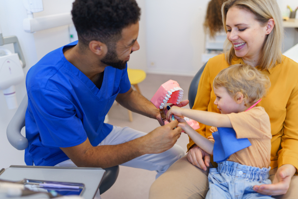 Young multiracial dentist showing a little girl how to clean teeth.