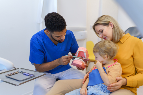 Young multiracial dentist showing a little girl how to clean teeth.