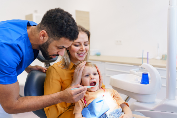 Little girl sitting with her mother on dentist chair, during preventive examination in dental clinic.