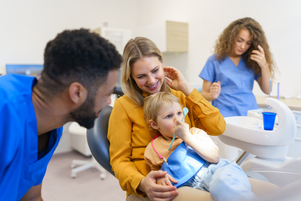 Young mother with her little daughter sitting at dentist chair, in his office at dental clinic.