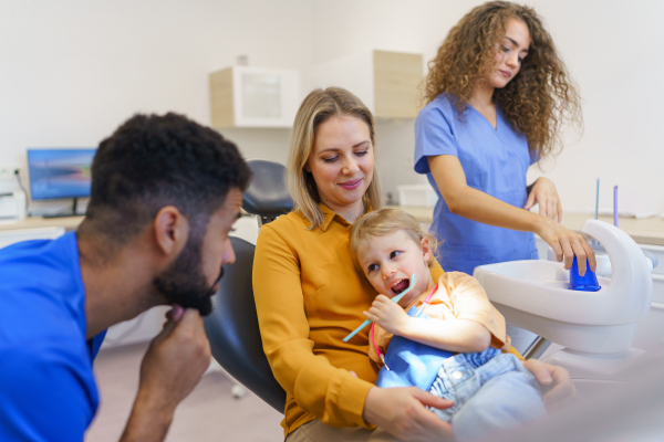 Little girl sitting with her mother on dentist chair, during preventive examination in dental clinic.