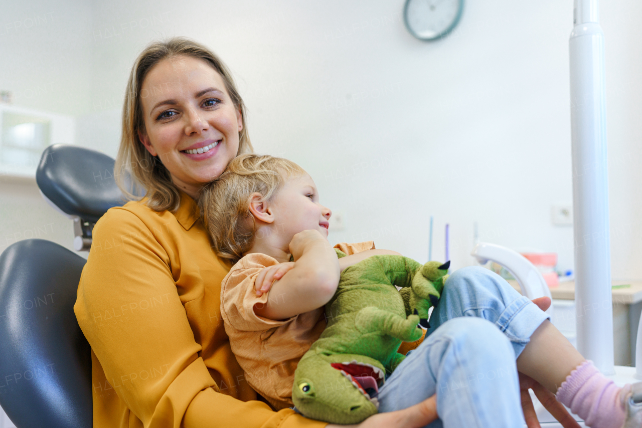 Portrait of young mother with her little daughter sitting at dentist chair, in his office at dental clinic.