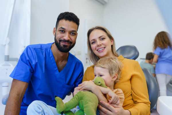 Portrait of multiracial dentist and young mother with little child on a dentists chair.