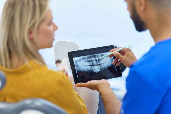 Rear view of dentist showing x-ray scan at digital tablet to patient.