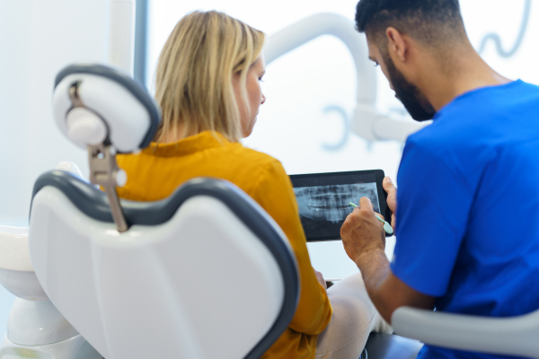 Rear view of dentist showing x-ray scan at digital tablet to patient.