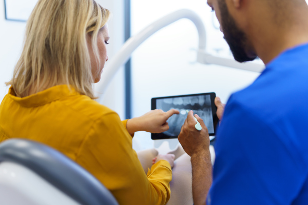 Rear view of dentist showing x-ray scan at digital tablet to patient.