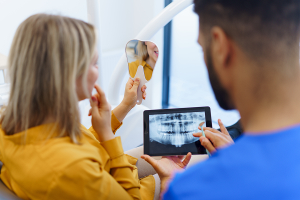 Rear view of dentist showing x-ray scan at digital tablet to patient.