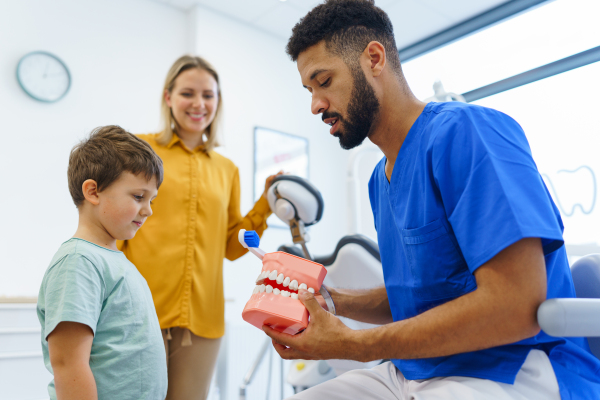 Young dentist showing little boy how to clean teeth, concept of children oral hygiene, prevention and dental health.