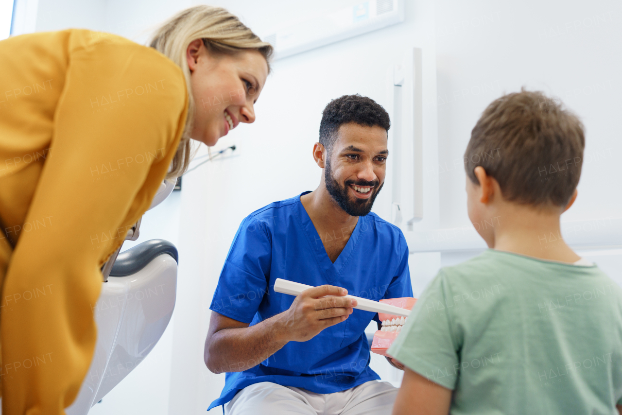 Young dentist showing little boy how to clean teeth, concept of children oral hygiene, prevention and dental health.