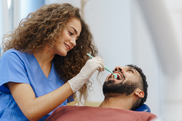 Young woman dentist doing preventive examination to the multiracial man.