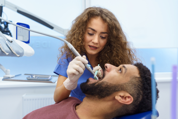 Young woman dentist doing preventive examination to the multiracial man.