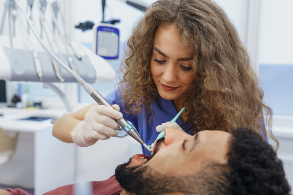 Young woman dentist doing preventive examination to the multiracial man.