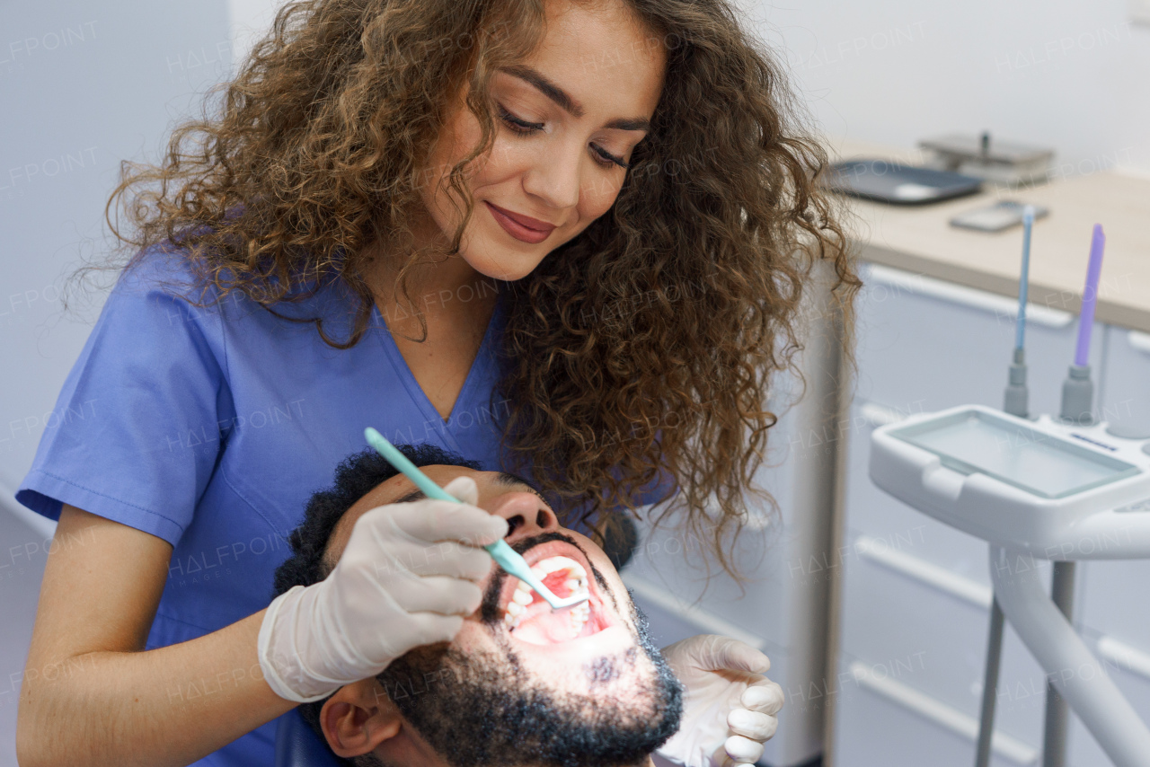 Young woman dentist doing preventive examination to the multiracial man.